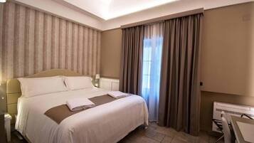 A hotel room with a large bed, a desk, and a window with curtains.