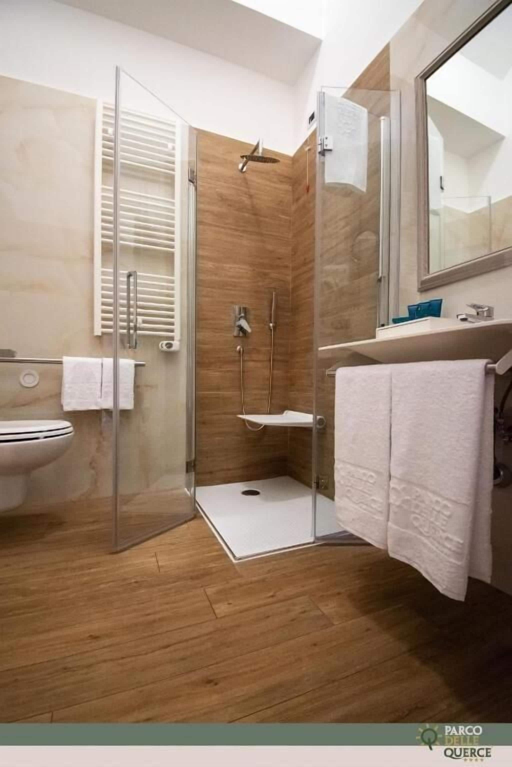 Ein modernes Badezimmer mit einer gläsernen Duschkabine, Holzboden und einem weißen Waschbecken.