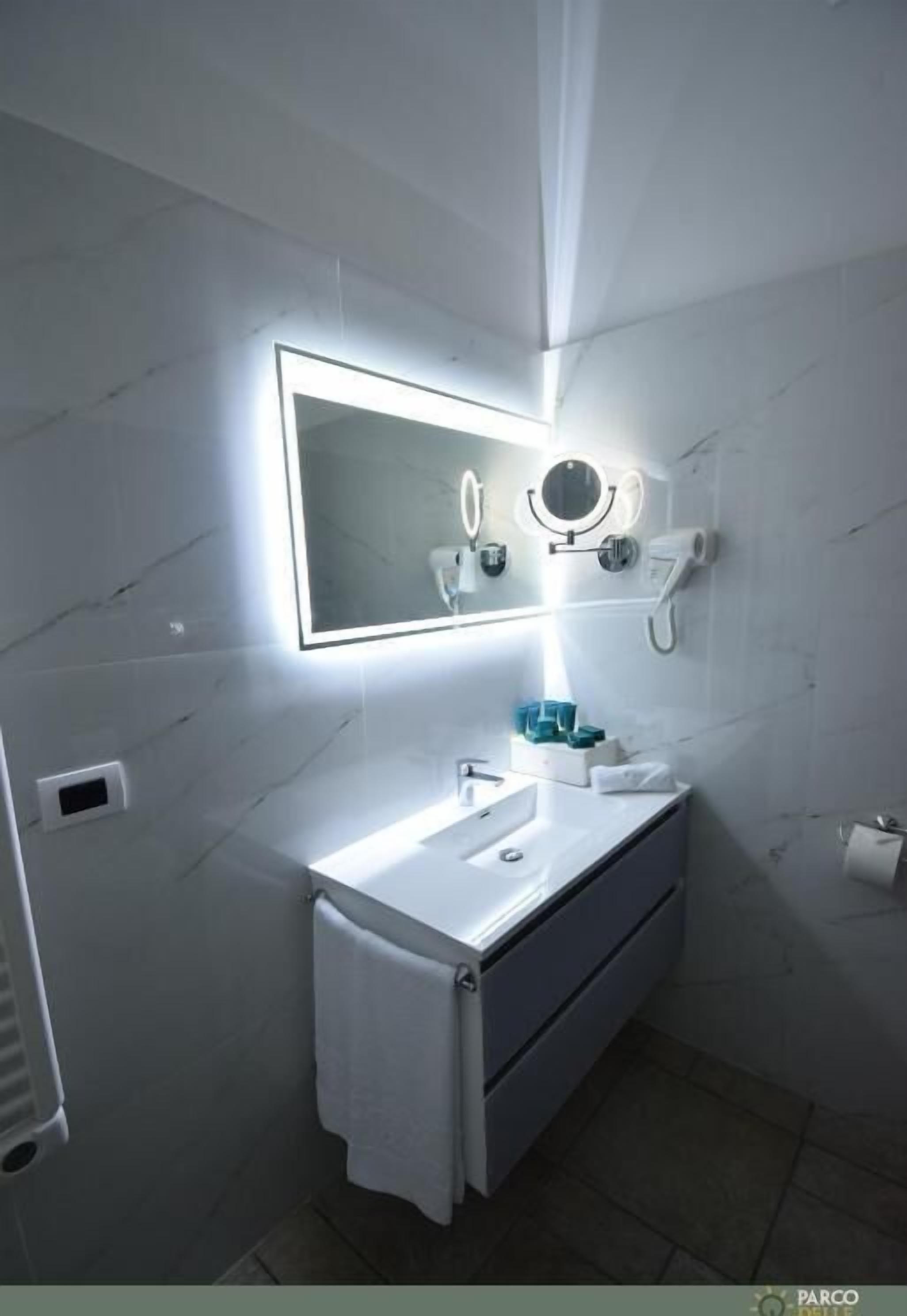 A modern bathroom with a white vanity, a large mirror with integrated lighting, a towel rack, and a toilet paper holder.