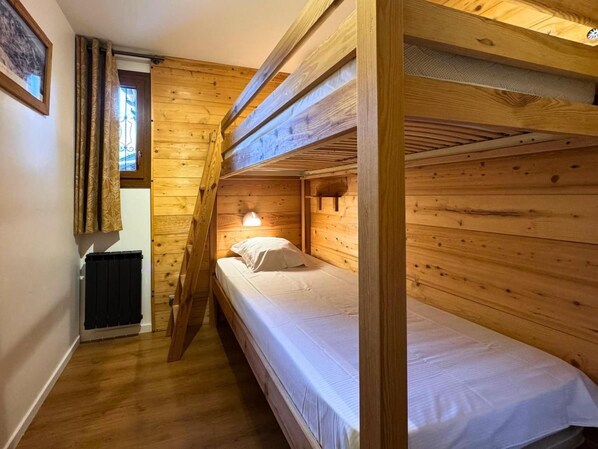 A bunk bed room with wooden walls, a radiator, and a window with curtains.