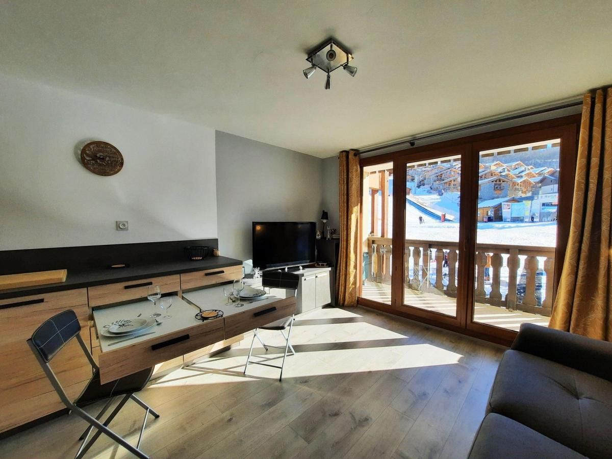 A modern kitchen with a dining area, a flat-screen TV, and a view of a snowy landscape through large windows.