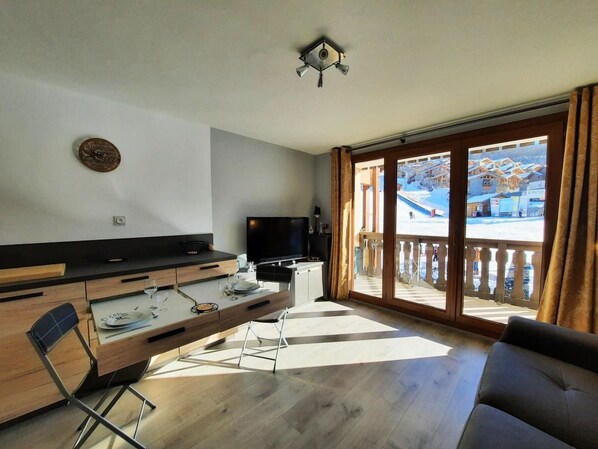 A modern kitchen with a dining area, a flat-screen TV, and a view of a snowy landscape through large windows.