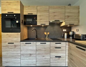 A modern kitchen with wooden cabinetry, a black microwave, a stainless steel kettle, and a toaster.