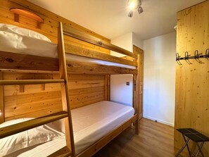 Habitación con literas, paredes de madera y una mesita pequeña.