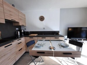 Una cocina moderna con una mesa de comedor para dos personas, una cafetera y un televisor de pantalla plana.