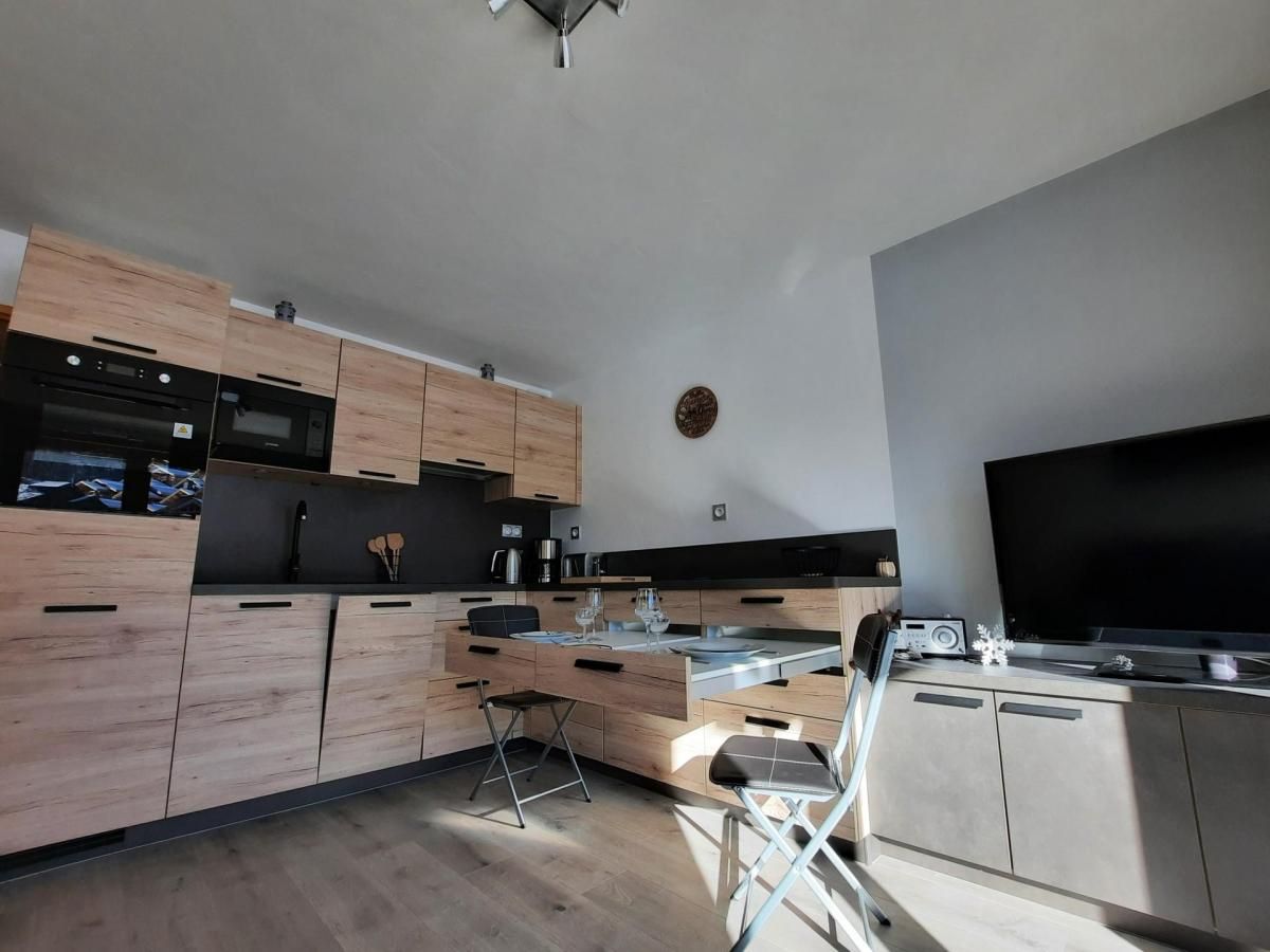 Eine moderne Küche mit Holzschränken, einer schwarzen Arbeitsplatte und einem großen Flachbildfernseher.