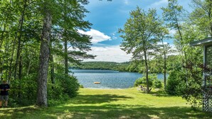 A lakeside view with a grassy area, trees, and a small dock. - Winnipesaukee Home PLUS Apartment For 10 Beach Dock Sunsets AUG 29TH SPECIAL (Moultonborough)