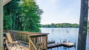 A wooden deck with a chair, a dock extending into a lake, surrounded by trees. - Winnipesaukee Waterfront in Meredith for 10 (Meredith)