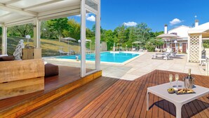 Una terraza de madera con piscina, mobiliario exterior y una mesa con bebidas.