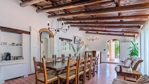 Un comedor con mesa y sillas de madera, una lámpara de araña y vistas al exterior.
