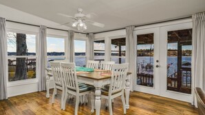 A dining area with a wooden table and white chairs, large windows with curtains, and a view of a lake. - READY TO RELAX?  Lake front house w/ beautiful Sunsets on Lake Greenwood (cross Hill)