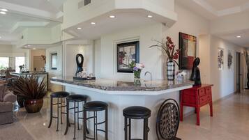 A modern kitchen with a central island, bar stools, a red side table, and decorative items.