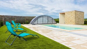 Une piscine dotée d’une structure en pierre, d’une pelouse verdoyante et de deux chaises longues bleues.