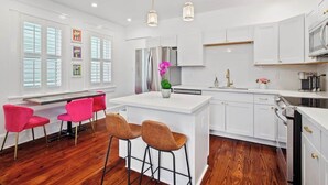 Una cocina moderna con armarios blancos, una isla central con taburetes y luminarias colgantes.