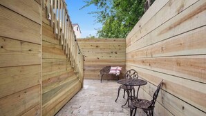 Un patio con cerramiento de madera, suelo de ladrillo, sillas metálicas y un banco.