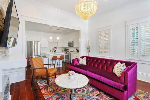 Open living room with fuchsia comfy couch, flat screen TV, and glam chandelier.