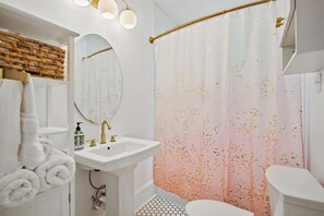 Une salle de bain avec un lavabo blanc, un miroir, un porte-serviettes et un rideau de douche parsemé de motifs dorés.