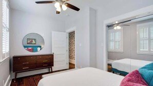 Un dormitorio con cama, cómoda, ventilador de techo, espejo y armario con puerta corredera.