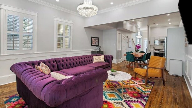 Una sala de estar moderna con un sofá púrpura, una araña y una alfombra colorida.