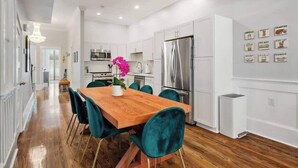 Una cocina moderna con armarios blancos, electrodomésticos de acero inoxidable y sillas color turquesa alrededor de una mesa de comedor de madera.