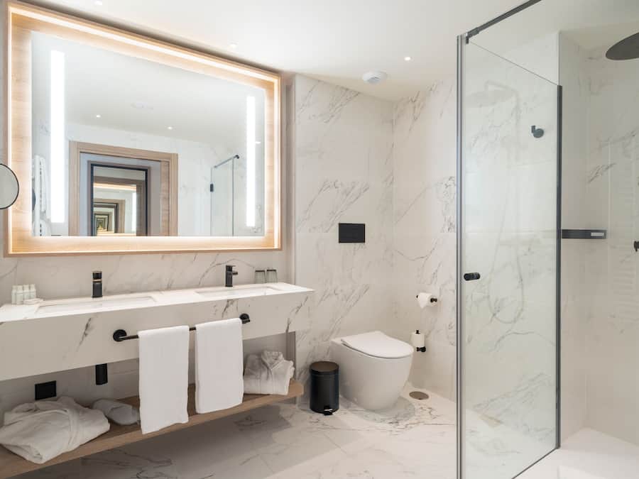 A modern bathroom with a large mirror, two sinks, a toilet, and a glass-enclosed shower.