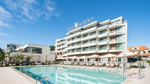 Un hotel moderno con piscina, varios balcones y cielo despejado.