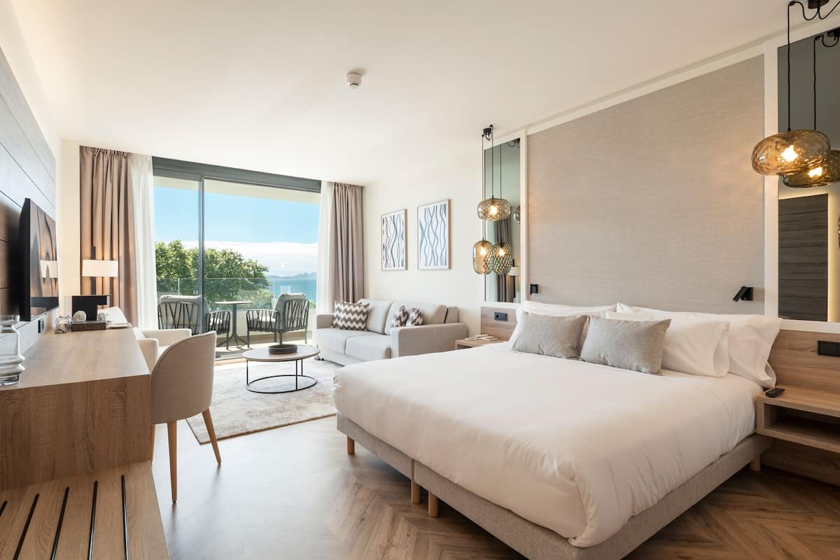 Quarto de hotel moderno com uma cama grande, uma escrivaninha e varanda com vista para o mar.