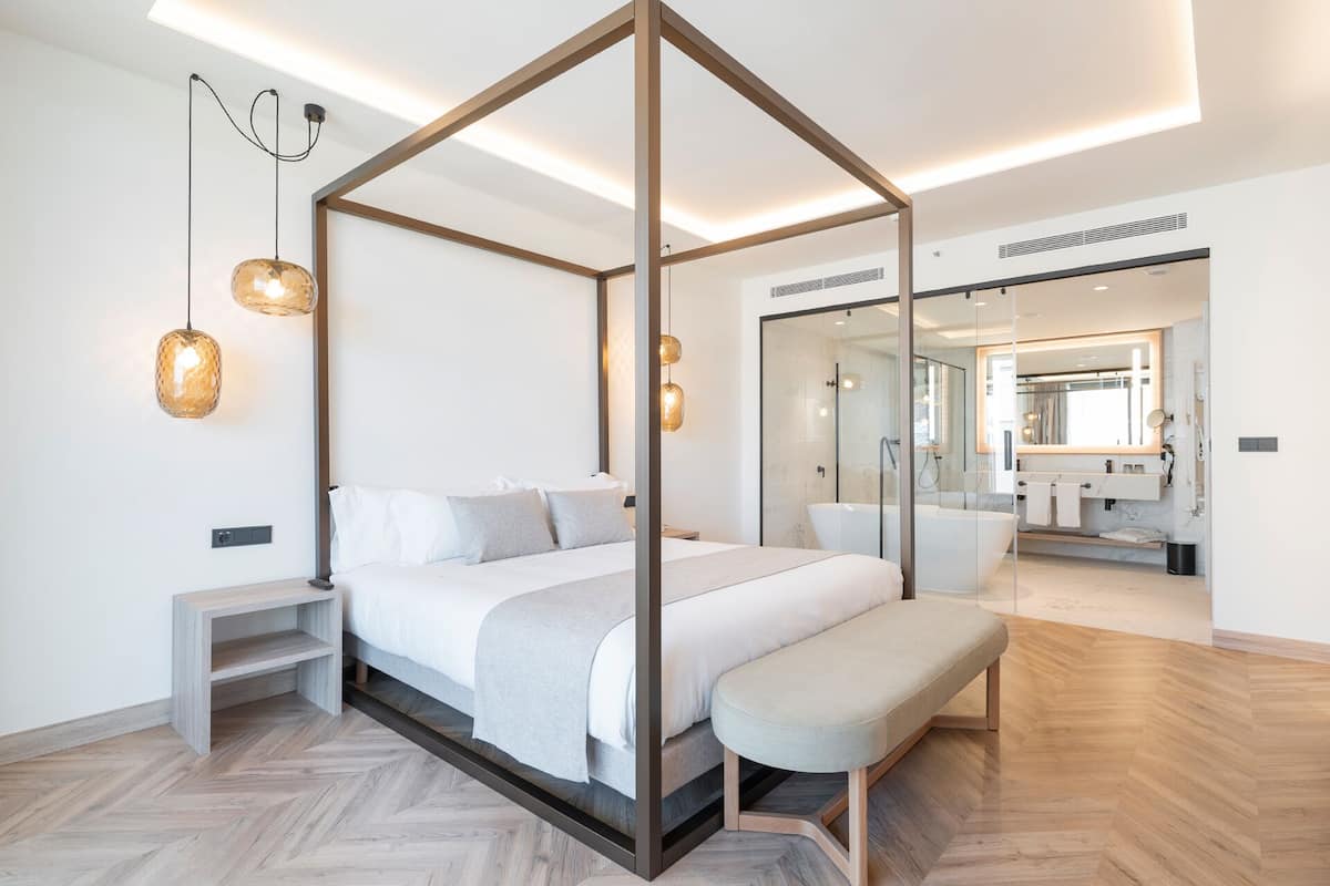 Quarto moderno com cama de dossel, mesas de cabeceira, um banco e um espelho grande.
