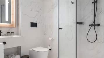 Un baño moderno con ducha envuelta en vidrio, piso de mármol, inodoro blanco y tocador con espejo.