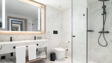 Un baño moderno con piso de mármol, un espejo grande, cabina de ducha con vidrio y tocador con lavamanos y perchero.