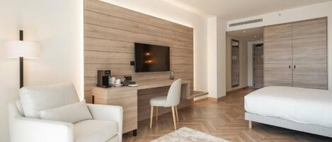 Una habitación de hotel moderna con sofá, escritorio con televisor de pantalla plana, cama y armario.