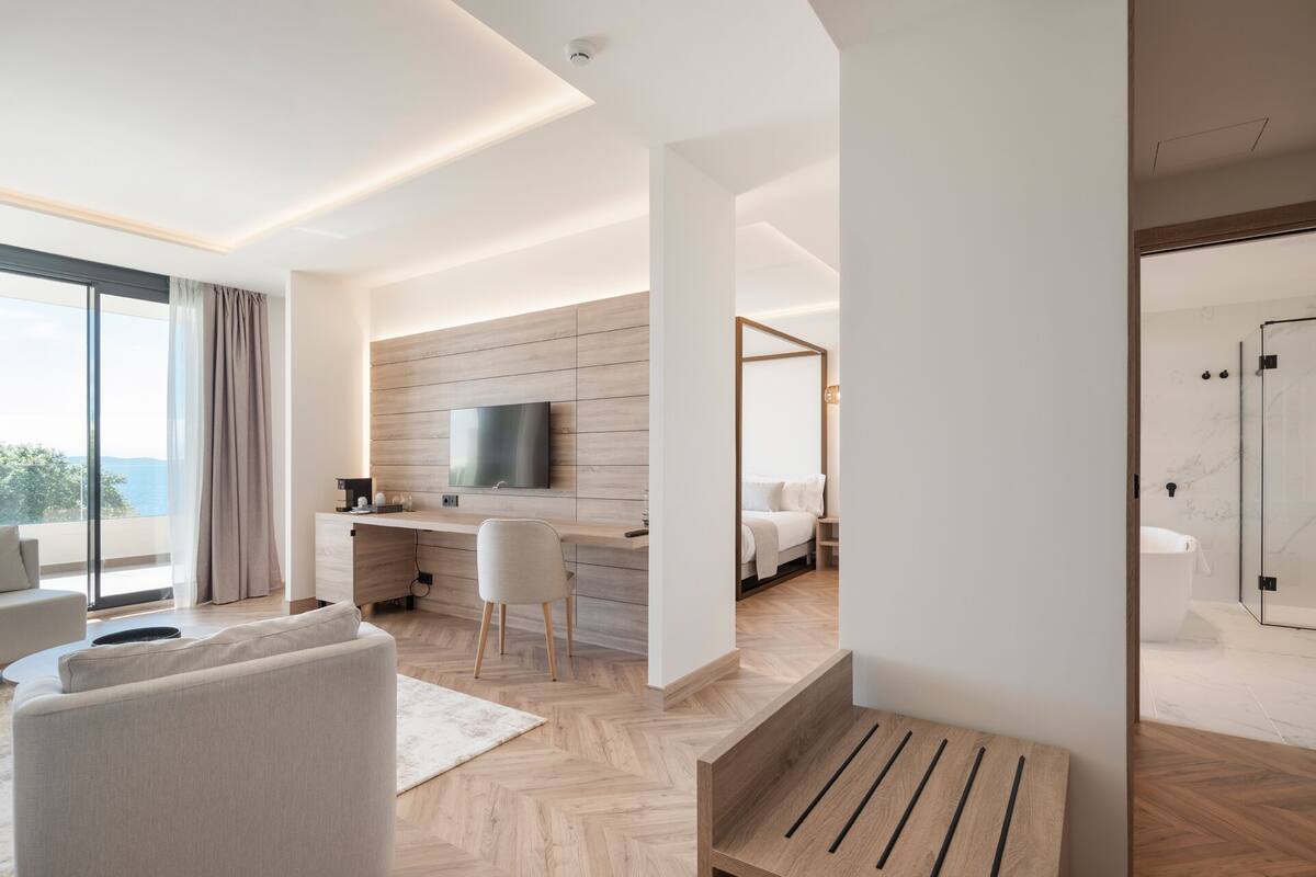 Quarto de hotel moderno com uma janela grande, televisão de tela plana, escrivaninha, cama e banheiro.