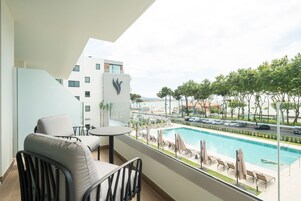 Un balcón con vistas a una piscina, sillas de descanso y un edificio moderno con un logotipo.
