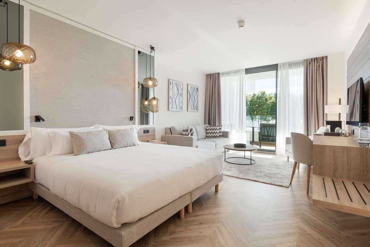 Quarto de hotel moderno com uma cama grande, uma escrivaninha, um sofá e uma varanda com vista.