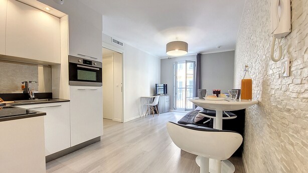 A modern kitchen with a built-in oven, a dining area with a round table and white chairs, and a white brick wall with a telephone. - N&J - LE SALEYA - Old Town - Very close sea (Niza)