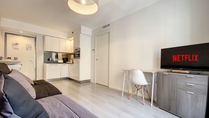 A modern living room with a sofa, a television displaying 'NETFLIX', a dining area with a table and chairs, and a kitchen in the background. - N&J - LE SALEYA - Old Town - Very close sea (Niza)