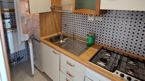 Eine Küche mit weißen Schränken, einer Spüle aus Edelstahl, einem Gasherd und einem Fliesenspiegel mit Muster.
