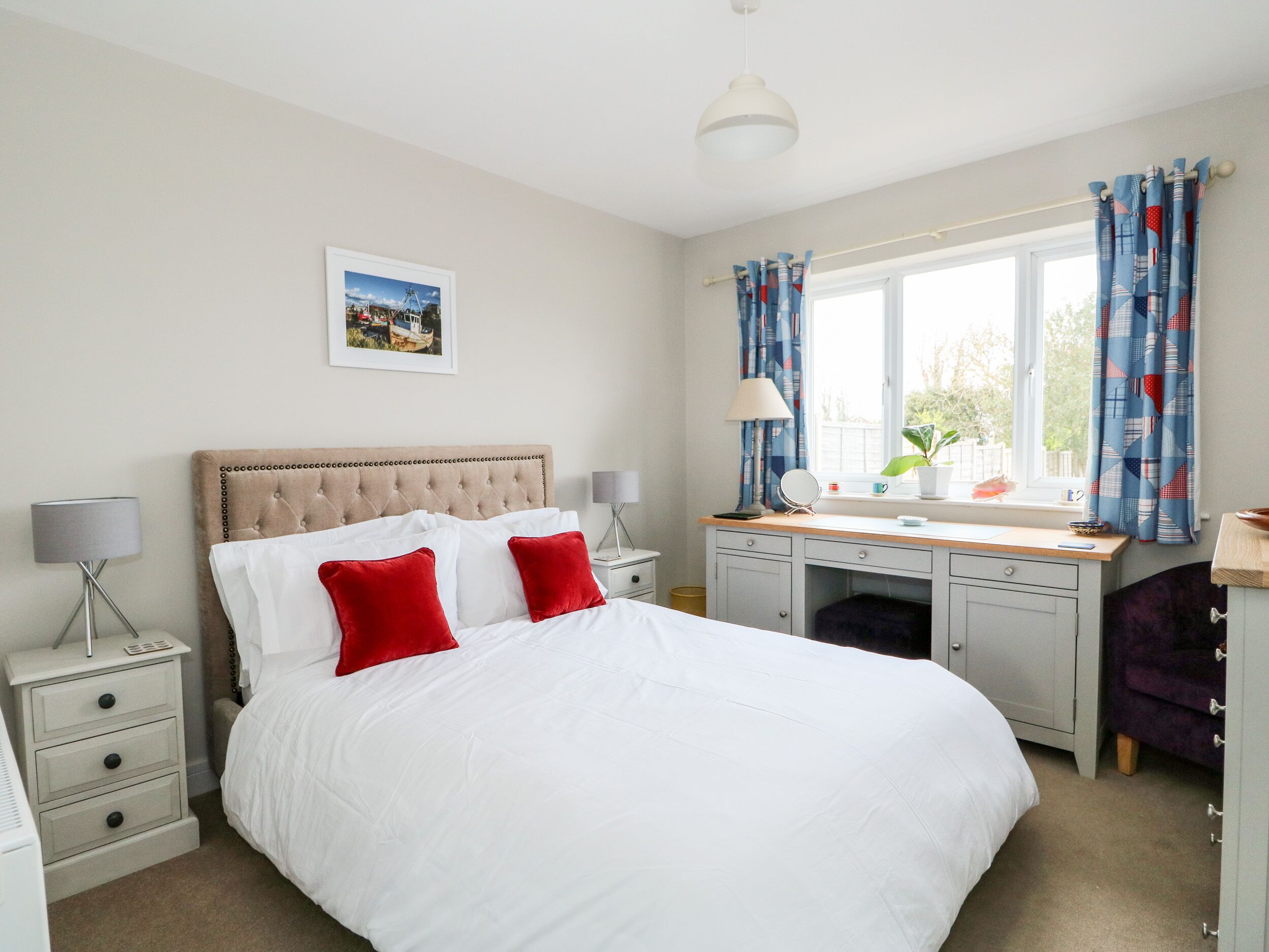 A bedroom with a bed, bedside tables, a desk, and a window with curtains.
