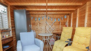 L’intérieur d’un chalet accueillant, avec un canapé gris, des fauteuils à motifs jaunes, une petite table ronde et un réfrigérateur.