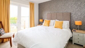 Une chambre avec un grand lit, deux lampes de chevet, une table de nuit en bois, une chaise et une vue sur l’extérieur grâce à une porte coulissante.