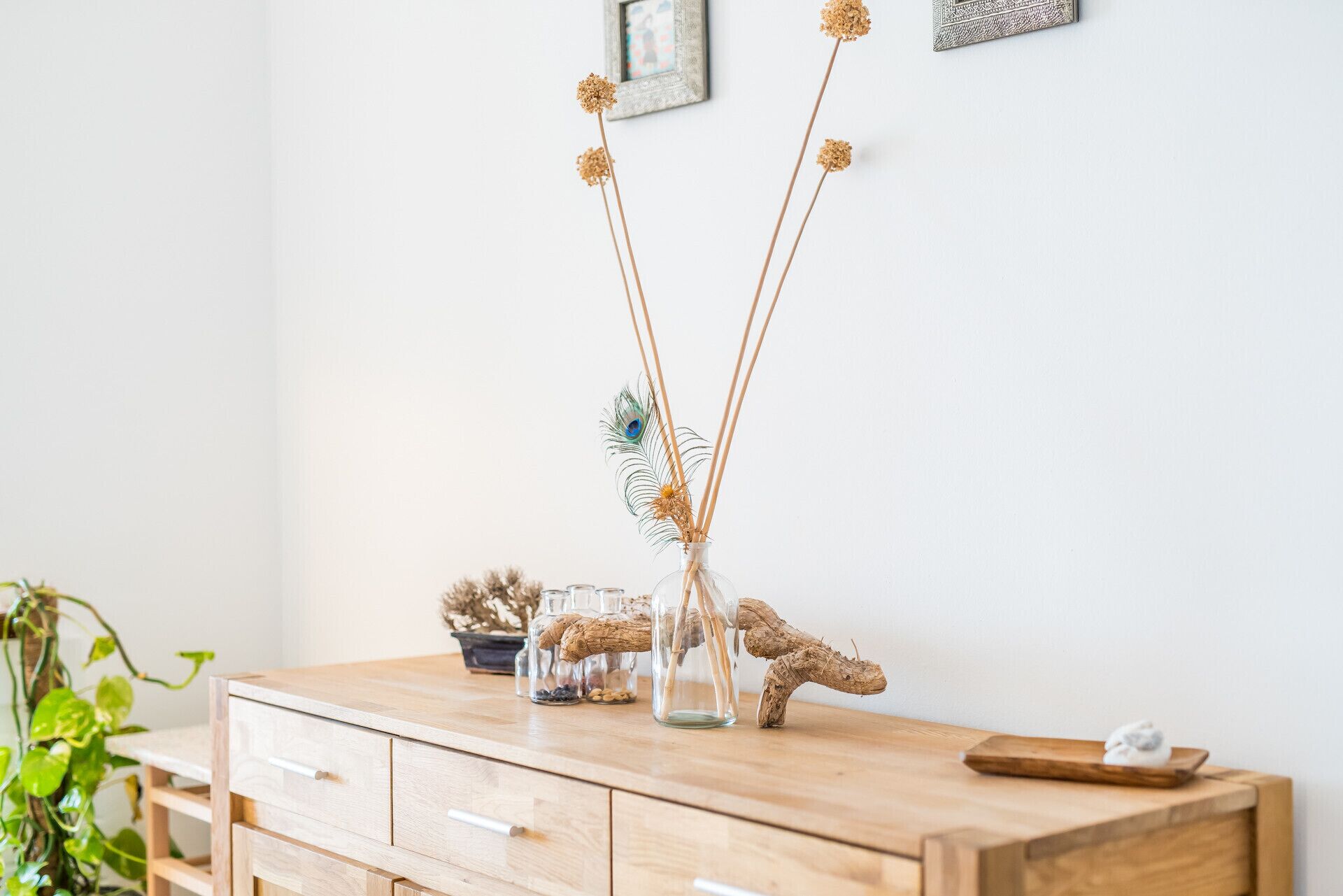 A wooden dresser with a glass vase containing dried flowers and a peacock feather.