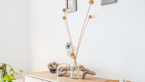 Un aparador de madera con un florero de vidrio que contiene flores secas y una pluma de pavo real.