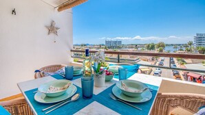 Un balcón con una mesa dispuesta para dos personas, con vistas a la ciudad y al agua.