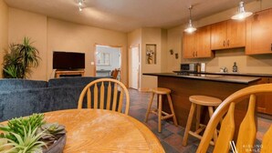 A modern kitchen with wooden cabinets, a dining area with a round table and chairs, a bar area, and a living room with a sofa and television. - Paddlers Inn - Guide's Suite | Rustic | Charming (Canal Flats)