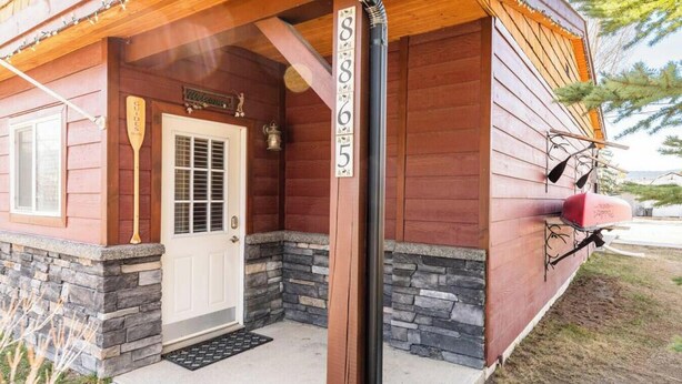 A wooden cabin with a stone foundation, a white door, and a welcome sign. - Paddlers Inn - Guide's Suite | Rustic | Charming (Canal Flats)
