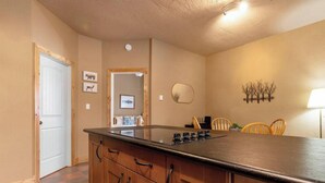 A kitchen with a central island, wooden cabinets, a white door, and a dining area with chairs. - Paddlers Inn - Guide's Suite | Rustic | Charming (Canal Flats)