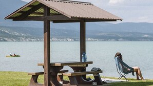 A wooden gazebo with a picnic table and a chair, overlooking a lake with kayaks in the distance. - Paddlers Inn - Guide's Suite | Rustic | Charming (Canal Flats)