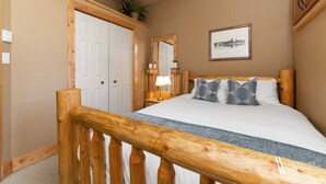 A bedroom with a wooden bed frame, a white door, a mirror, a bedside table with a lamp, and a framed picture on the wall. - Paddlers Inn - Guide's Suite | Rustic | Charming (Canal Flats)