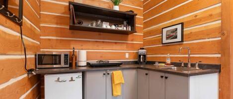 A compact kitchen with wooden paneling, a microwave, a coffee maker, and a sink.