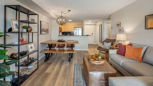 A modern living room with a sofa, coffee table, and a dining area with a wooden table and chairs. - Mountain Modern | Outdoor Pool | Hot Tub | Gym (Invermere)